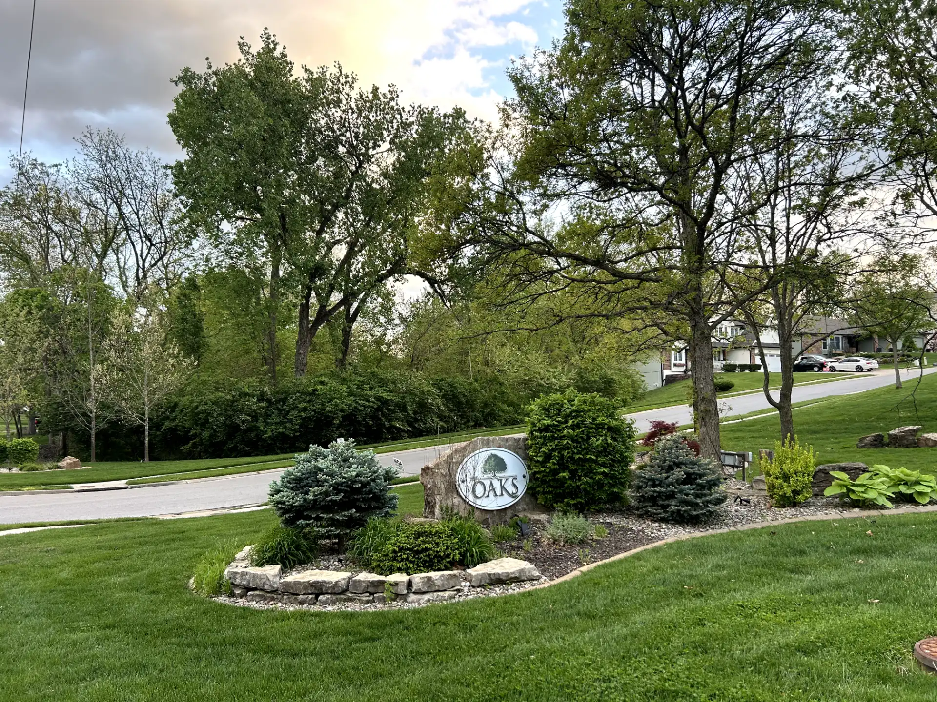 The Oaks neighborhood entrance with stone monument and landscaped trees